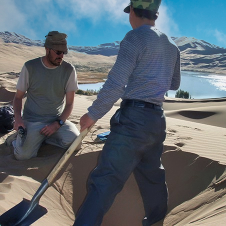 Two people digging a hole in the sand for research purposes.
