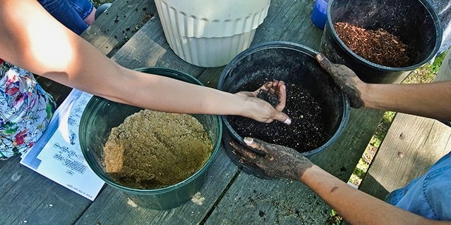 Three buckets with different types of soil with two people holding the buckets and feeling the soil.