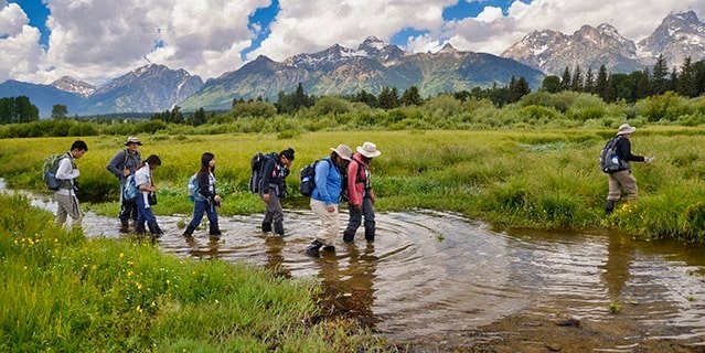 A group of teens hiking through water in the Rocky Mountains.
