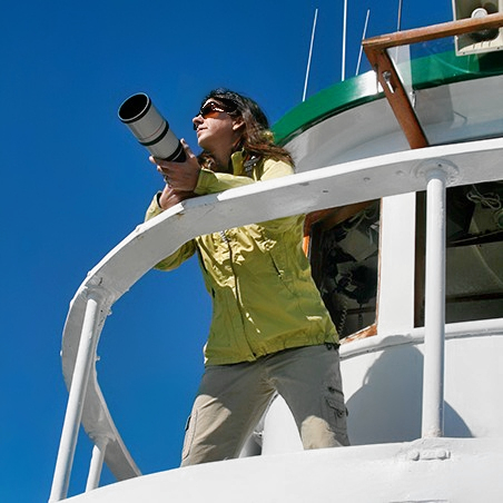 A woman at the bow of a boat holding a telescope.